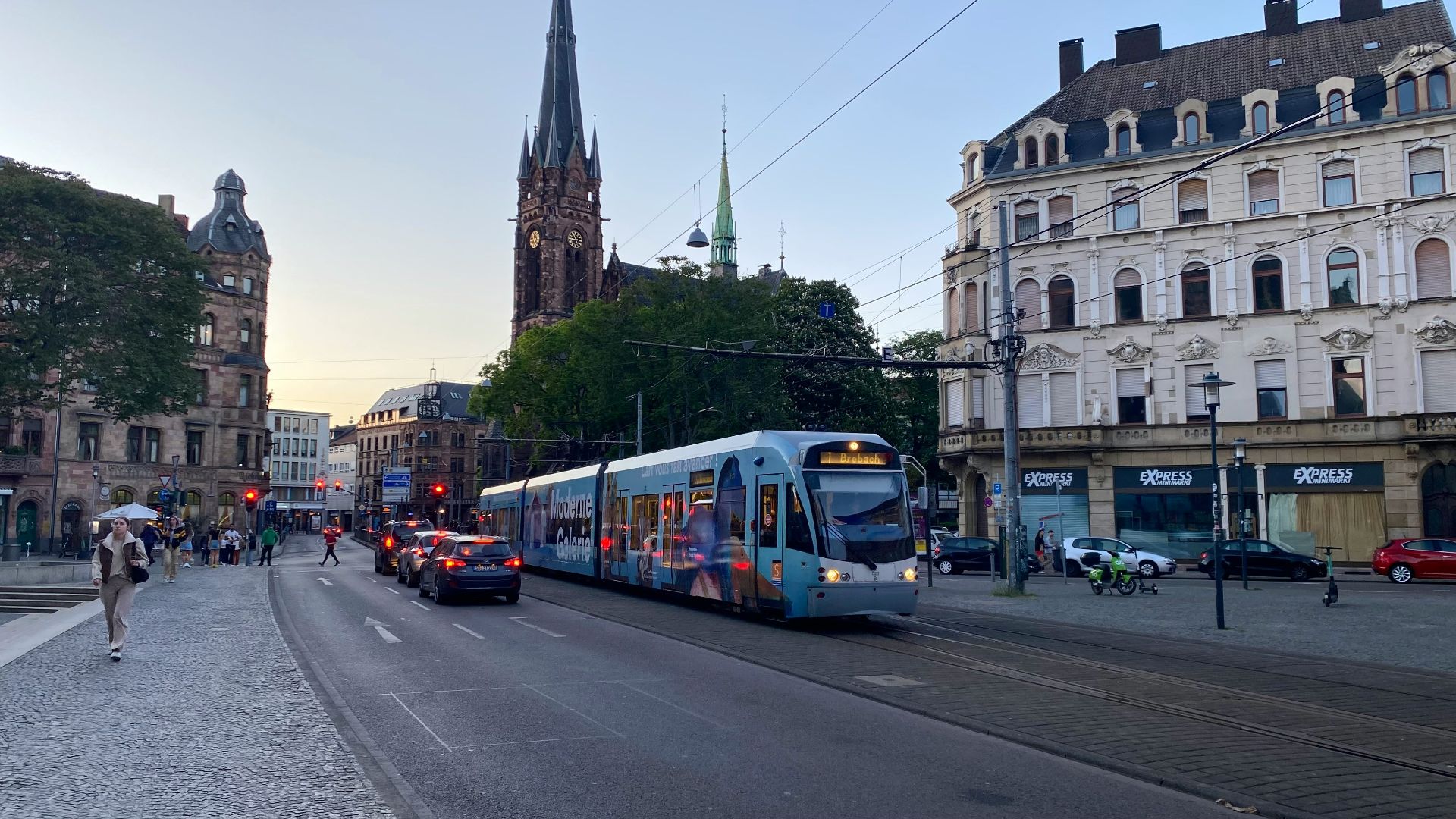 a blue and white train traveling down a street next to tall buildings