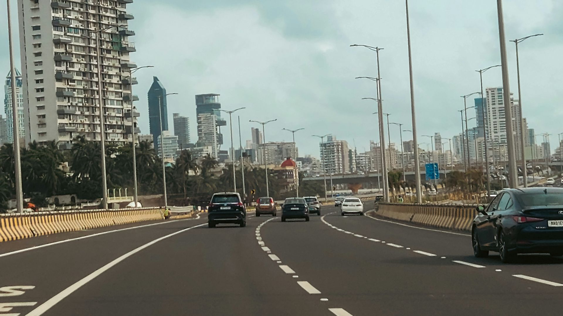 Cars drive on a city highway with tall buildings.