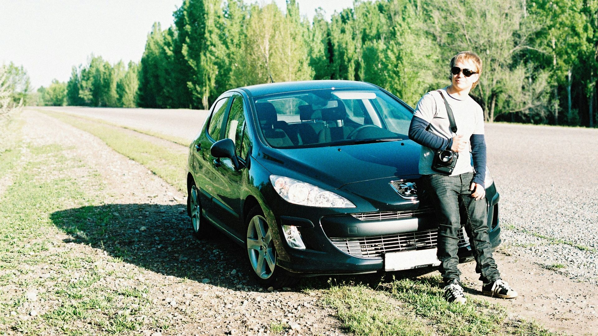 a man standing next to a car on a dirt road